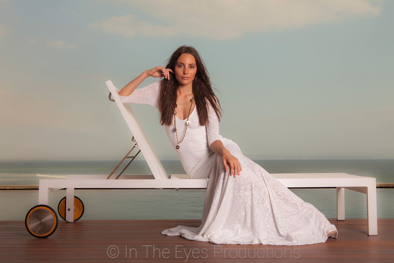 Woman in a long white dress reclining on a white sun lounger