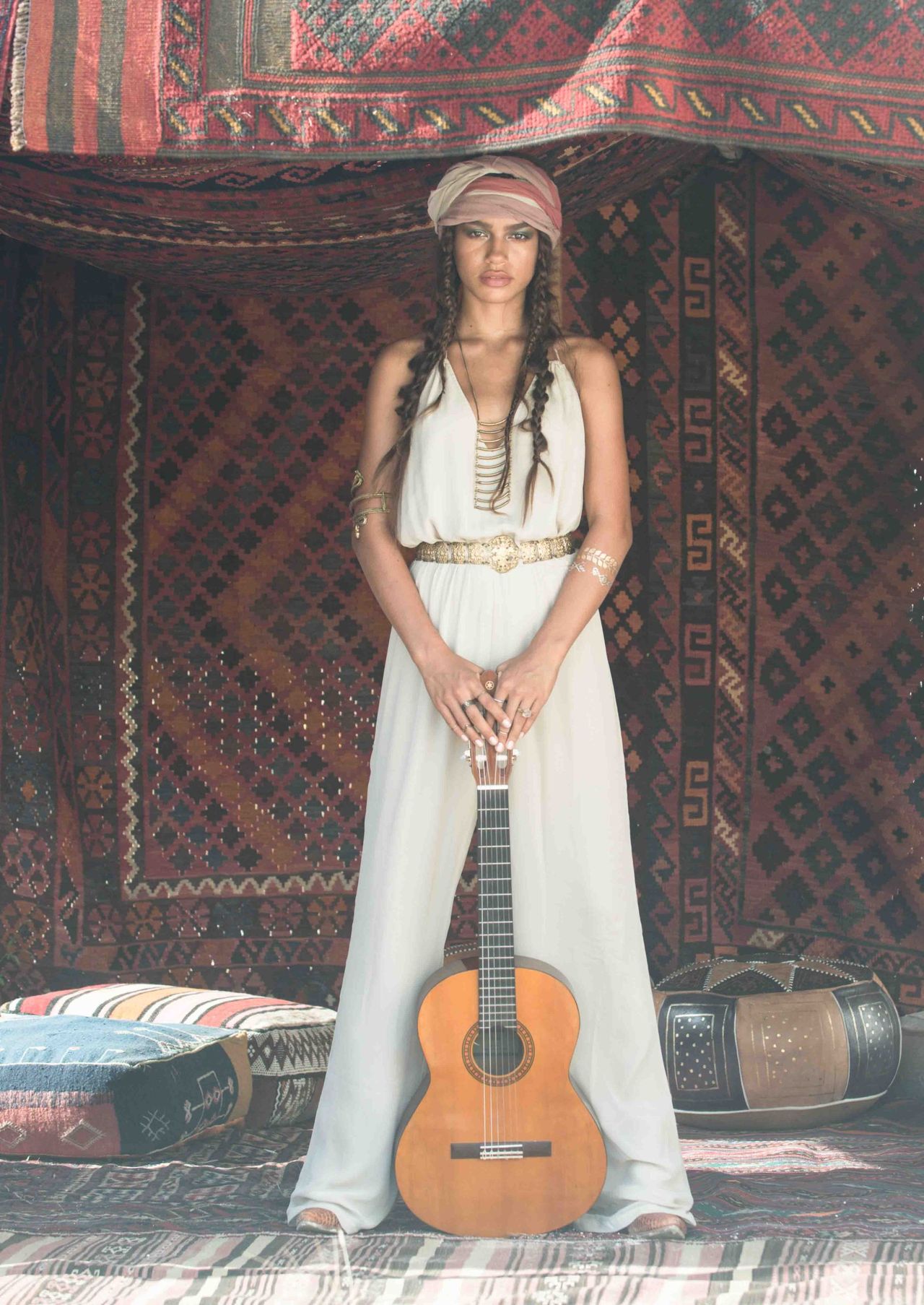 Woman in white with a guitar, standing in front of patterned rugs