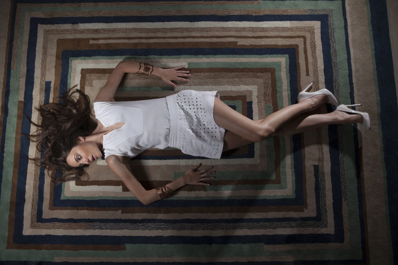 Woman in a white top lying on a patterned rug, seen from above