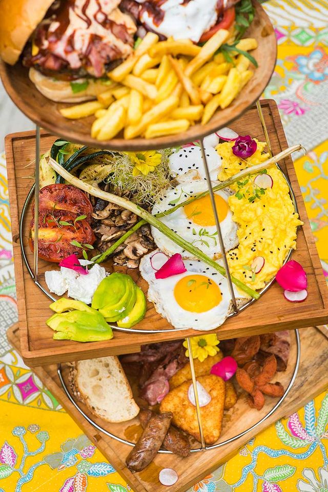 Tiered wooden stand of breakfast dishes with fried eggs, chips and a burger