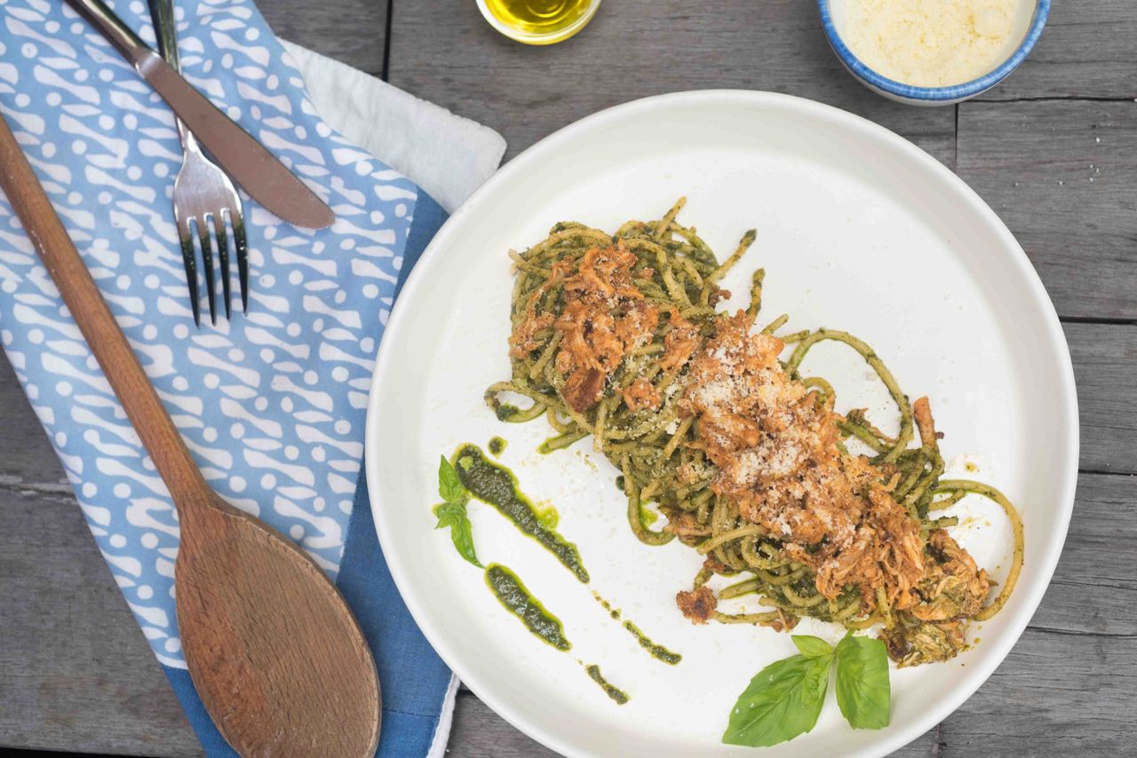 Pasta with pesto on a white plate beside a wooden spoon