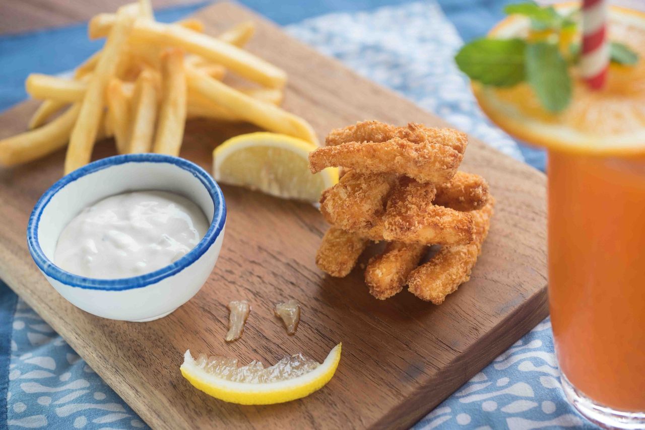 Fried chicken strips, chips, dipping sauce and an orange drink on a board