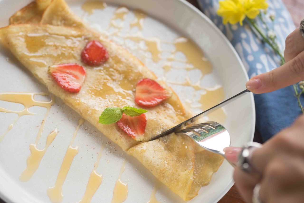 Crepe with strawberries and syrup on a white plate