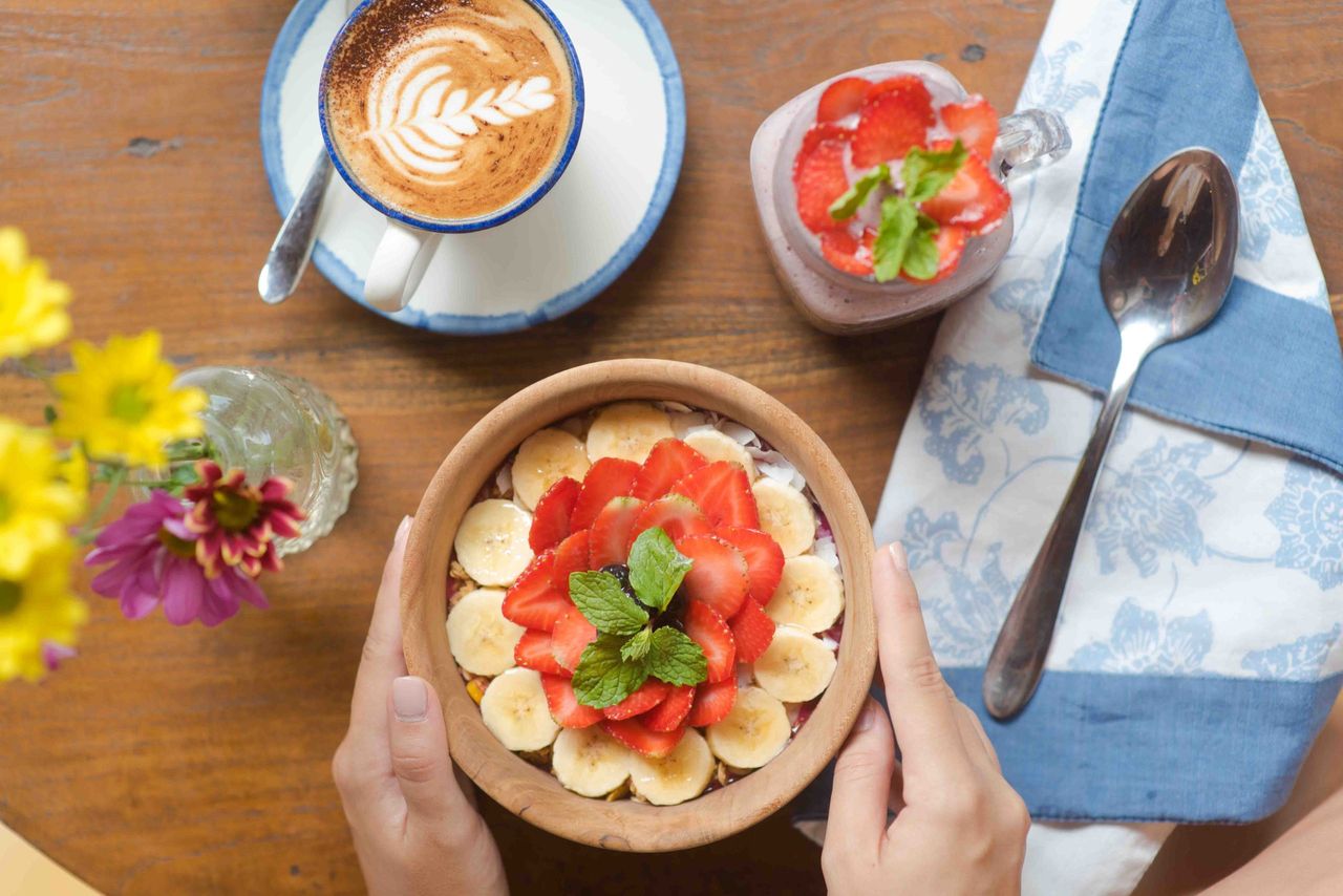 Smoothie bowl topped with banana and strawberries, with a latte