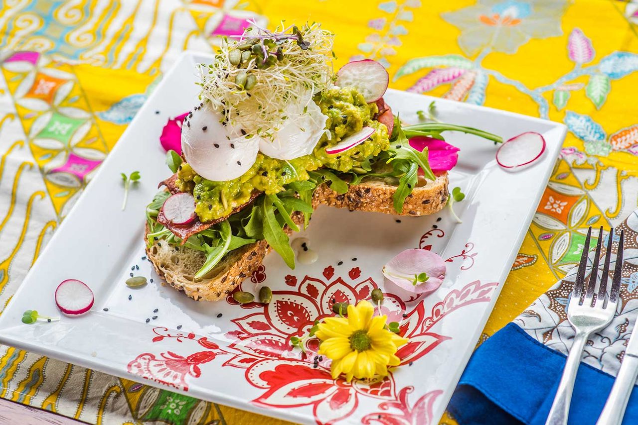 Open sandwich topped with sprouts and edible flowers on a patterned plate