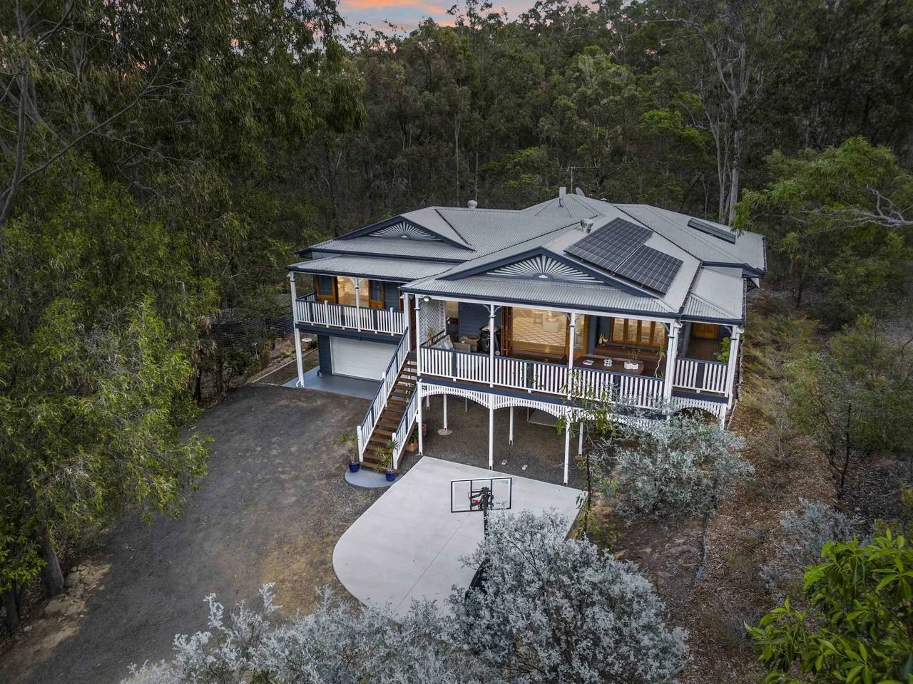 Aerial view at dusk of a Queenslander-style home with wraparound verandahs in bushland