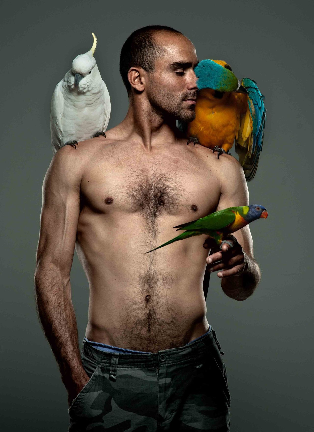 Shirtless man with a cockatoo, a macaw and a small parrot