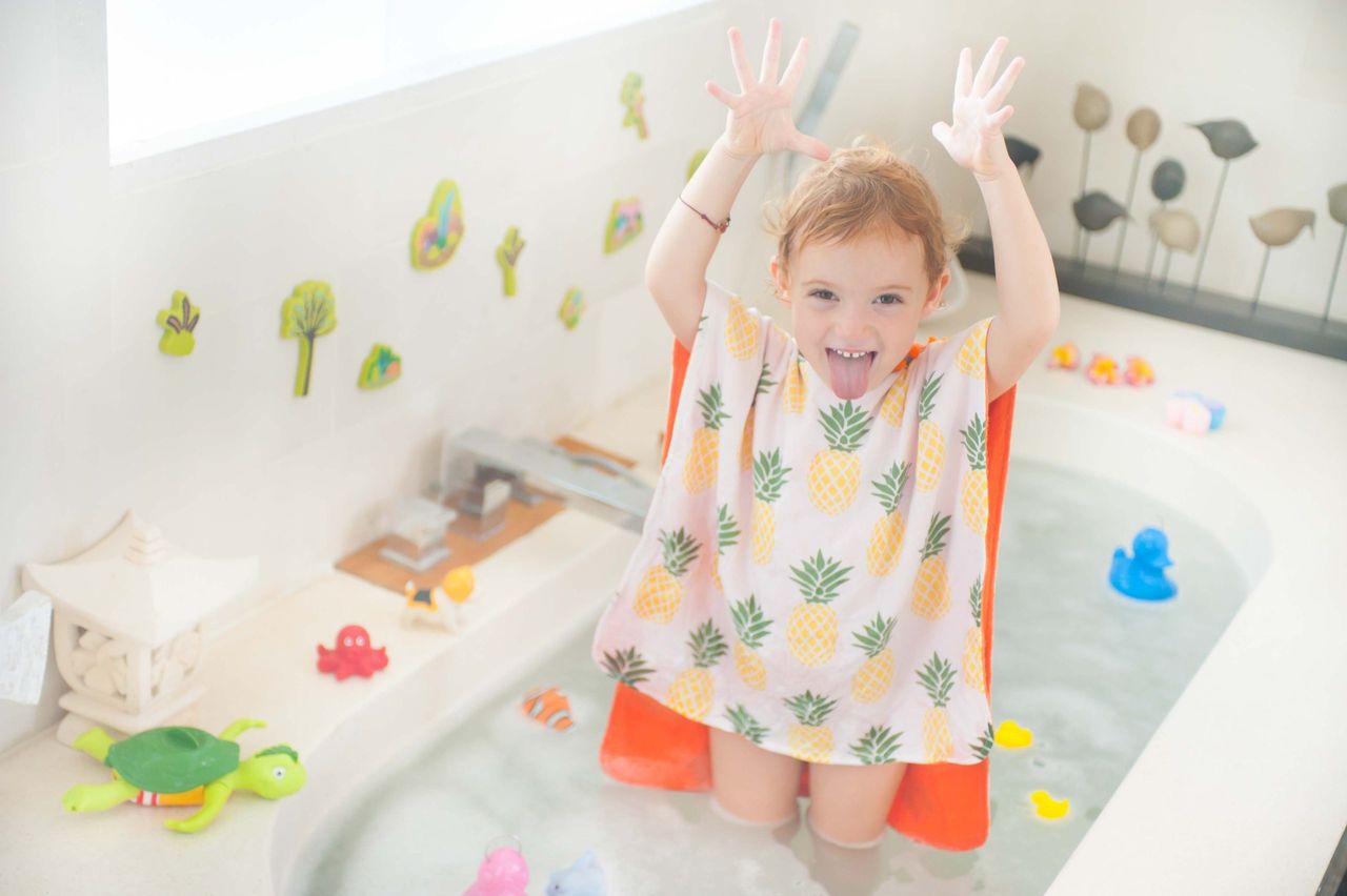Child in a pineapple-print poncho with arms raised in a bath