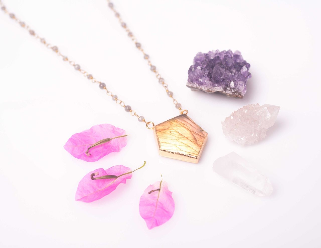 Pendant necklace beside amethyst crystals and pink petals