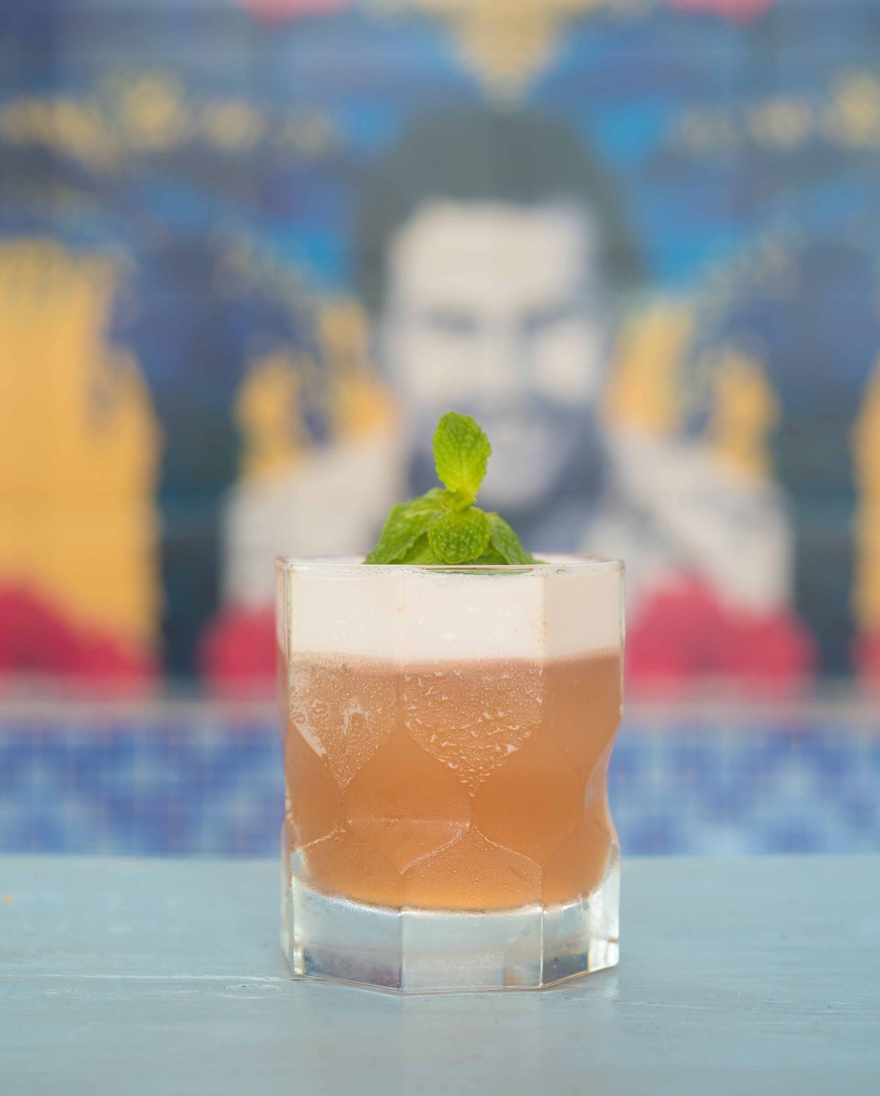 Amber drink with mint in front of a painted mural