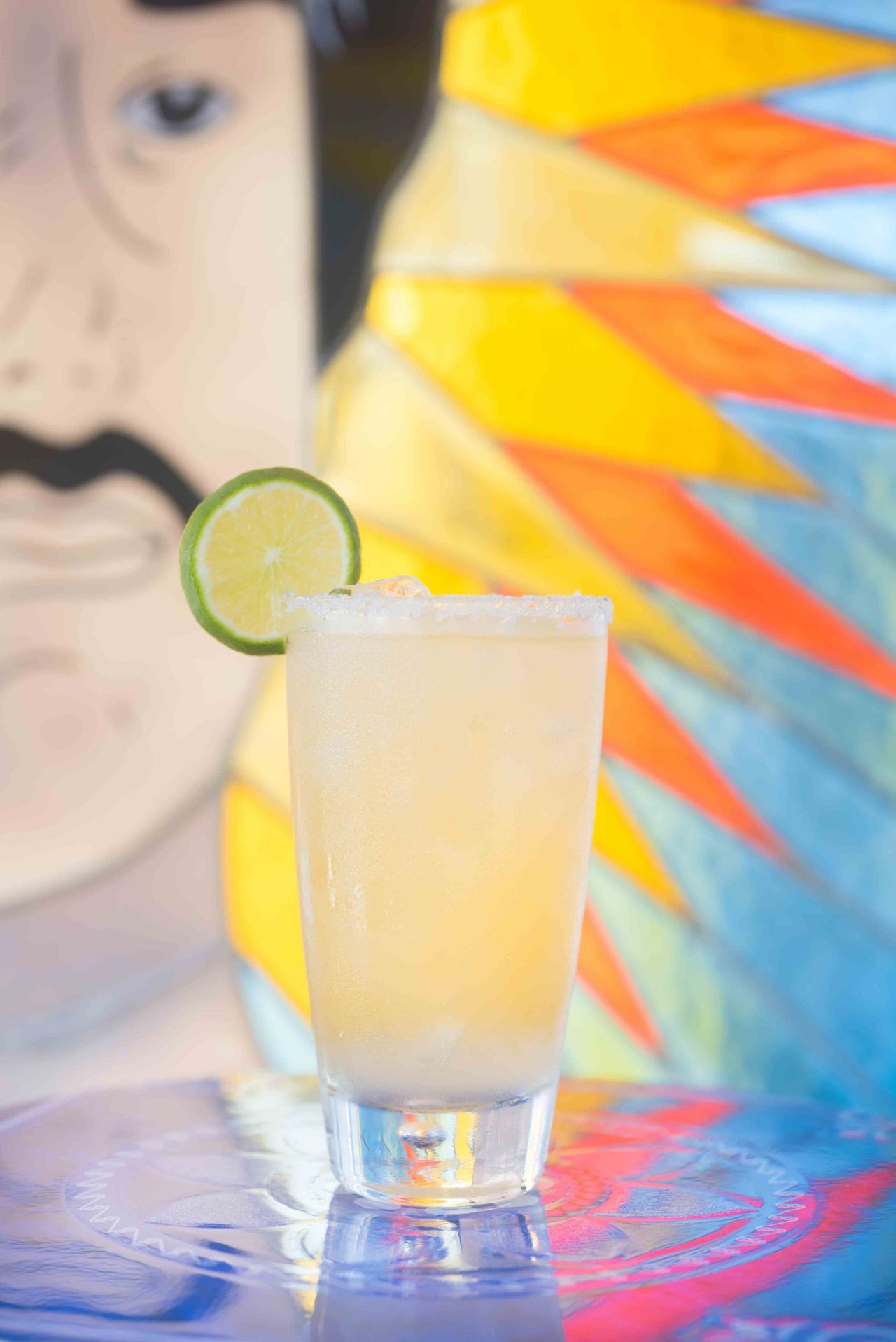 Pale drink with a lime slice in front of a painted mural