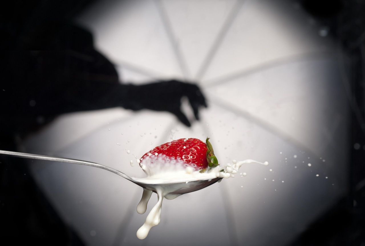 Strawberry on a spoon with milk splashing, beside a shadow of a hand