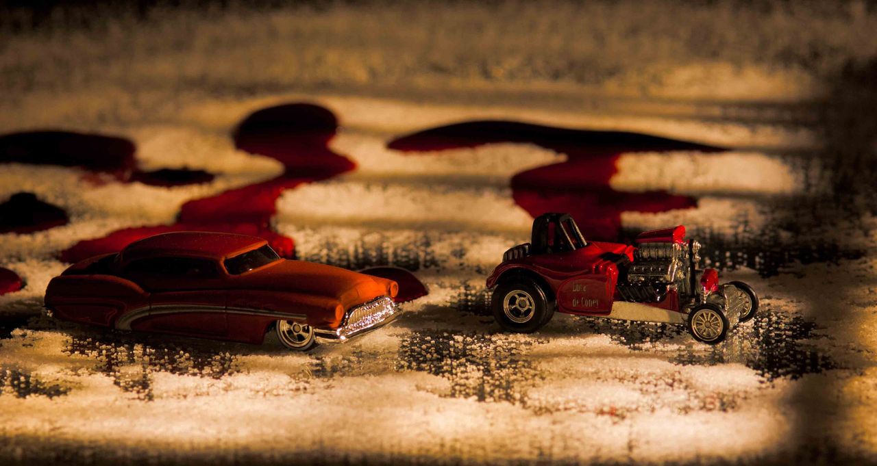 Two red toy cars on a textured surface in warm, moody light