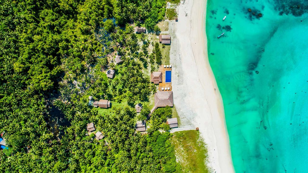 Aerial drone view of a white-sand beach, turquoise water and coastal forest