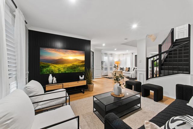 Open-plan living room with a black feature wall, wall-mounted TV, sofas and a black staircase