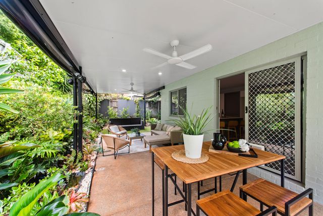 Covered timber deck with a dining table, potted plants and a ceiling fan