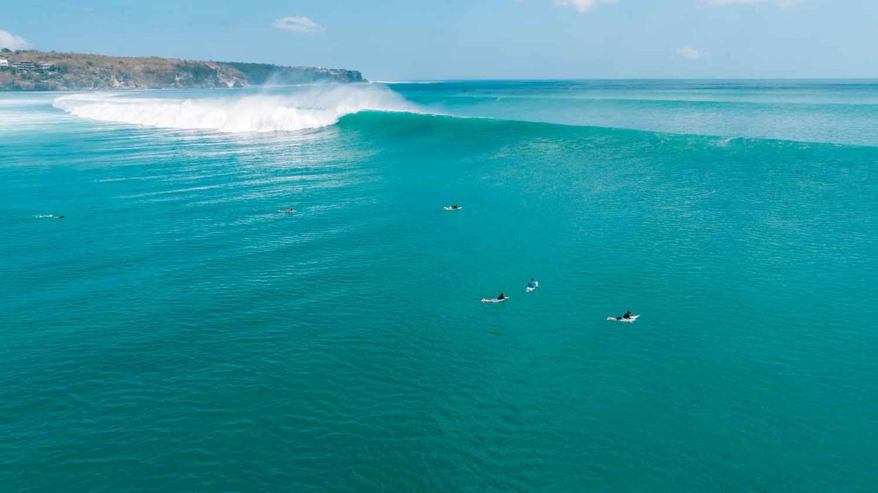 Surfers waiting for a wave in turquoise water near a headland