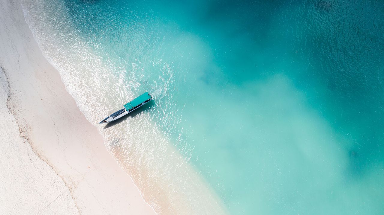 Aerial view of a small boat in shallow turquoise water off a white beach