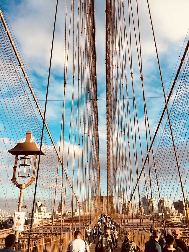 Looking up at the suspension cables and stone tower of a bridge