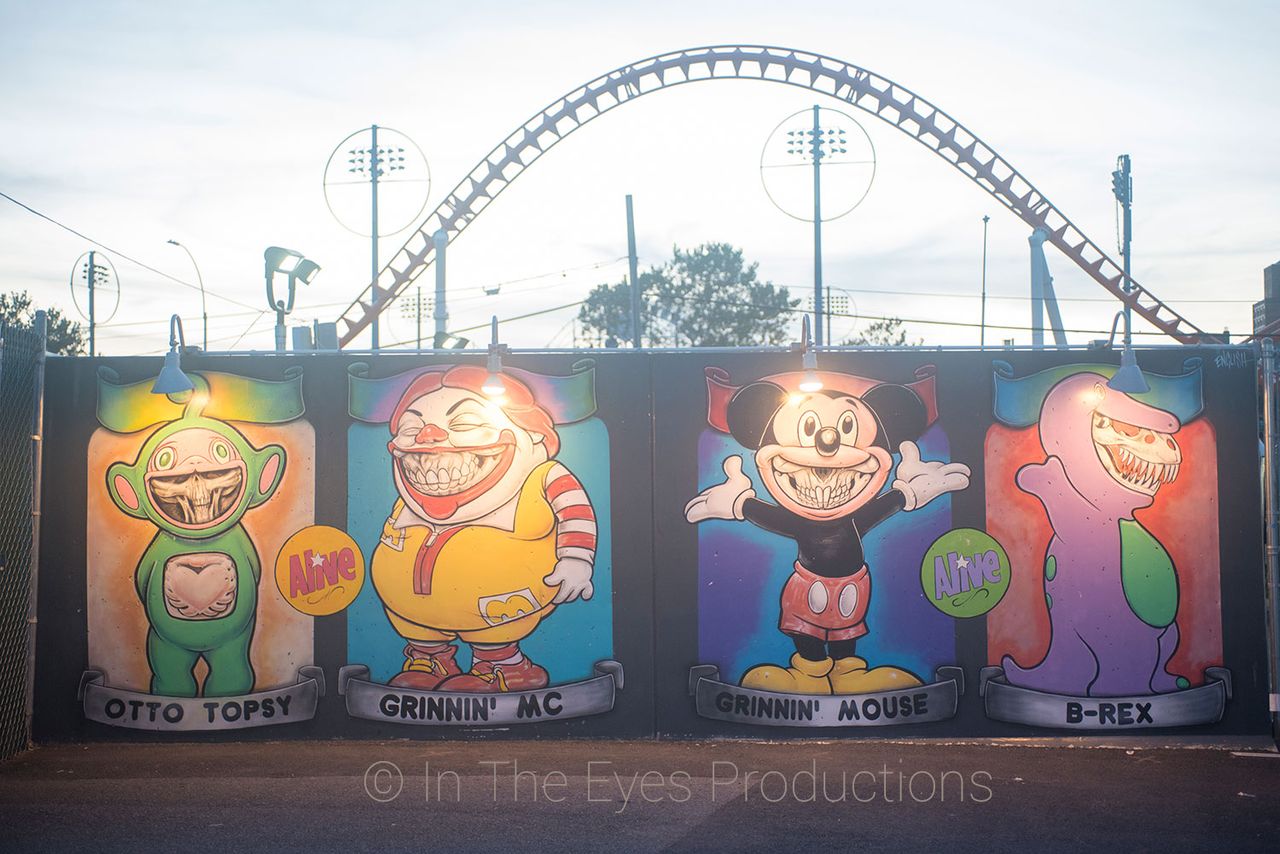 Painted cartoon mural on a wall beneath a roller coaster
