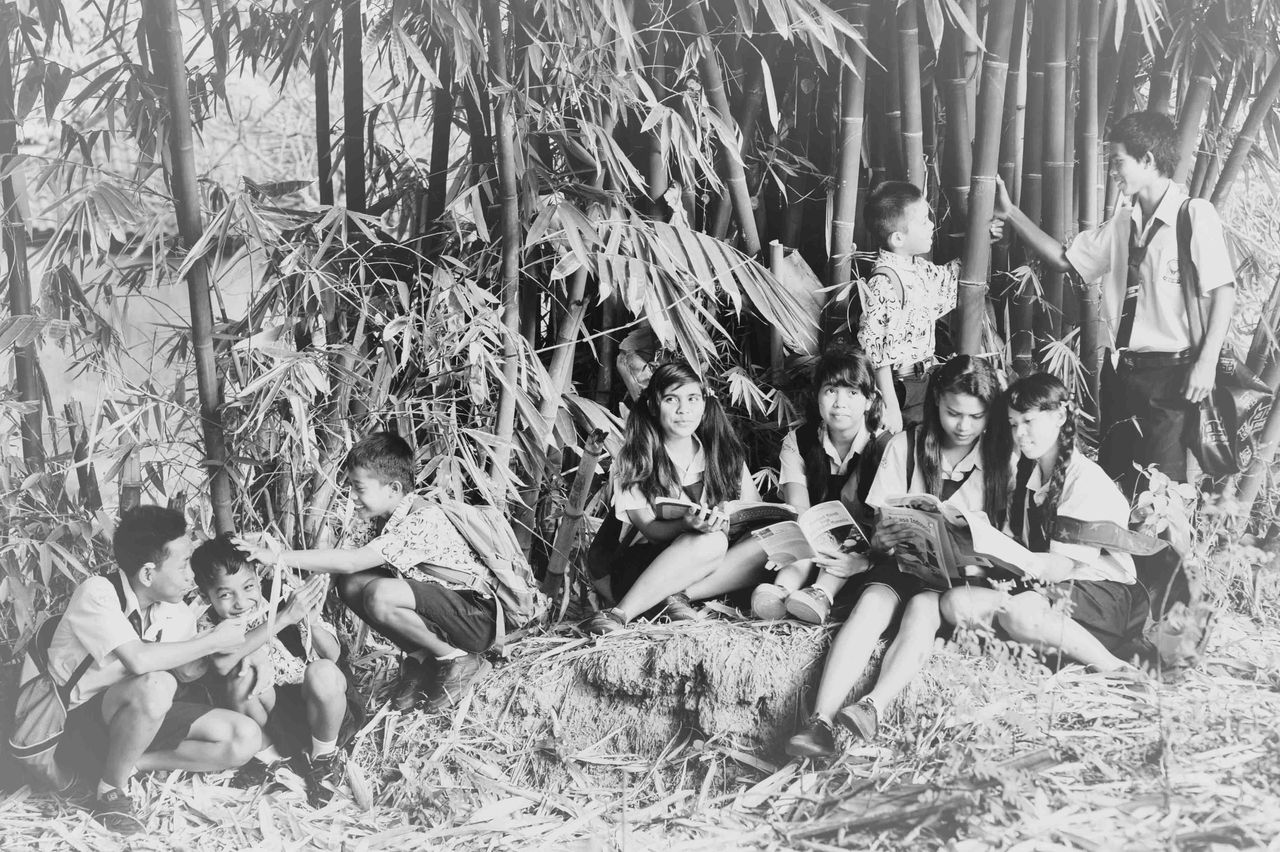 Black-and-white photo of a group of children sitting among bamboo