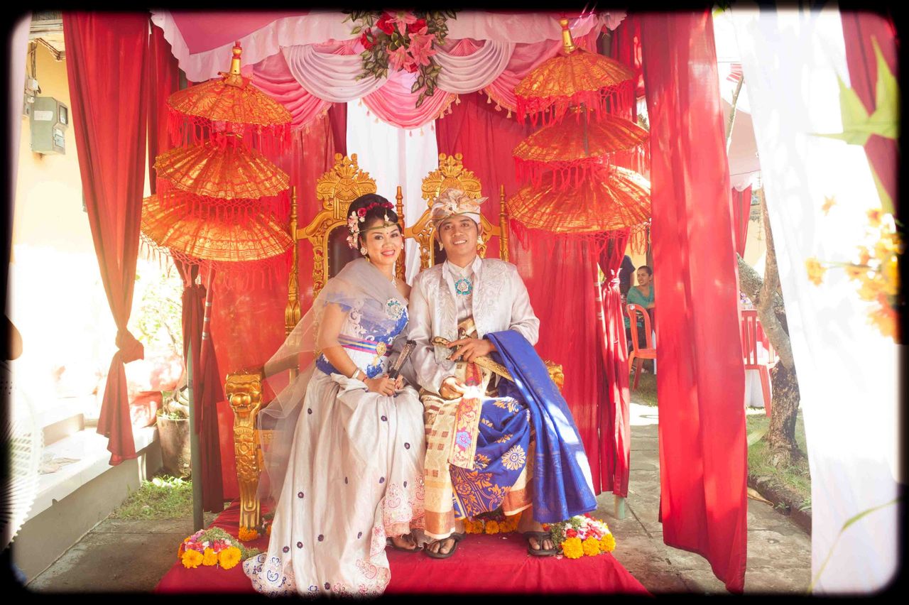 Couple in traditional wedding dress seated under red and gold decorations
