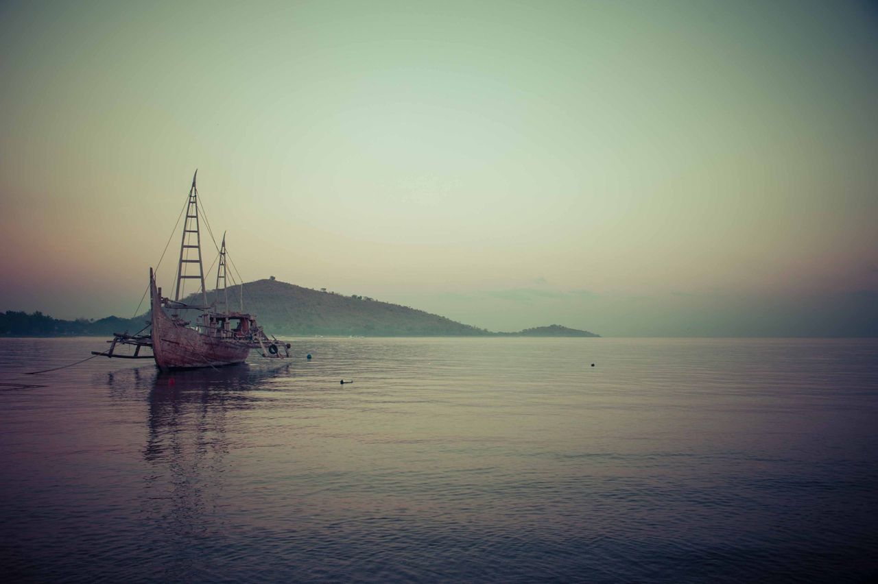 Traditional sailing boat on calm water at dusk, with hills behind