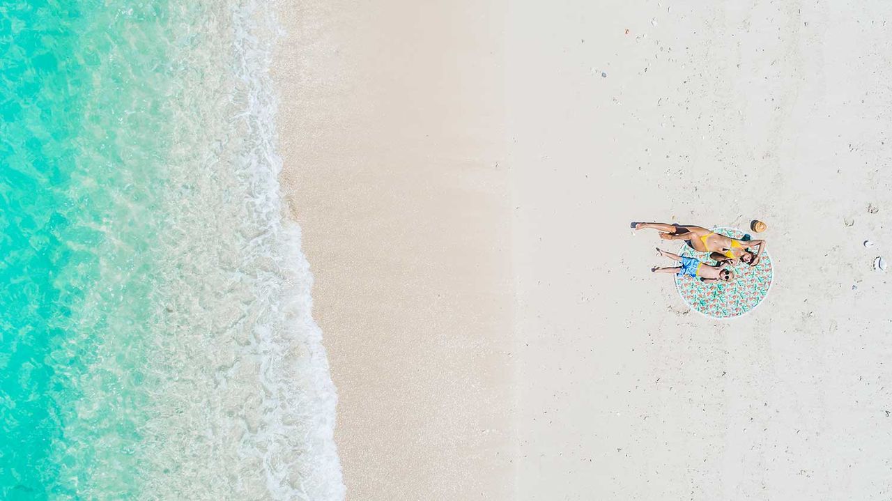 Aerial view of a person lying on a beach towel beside the waves