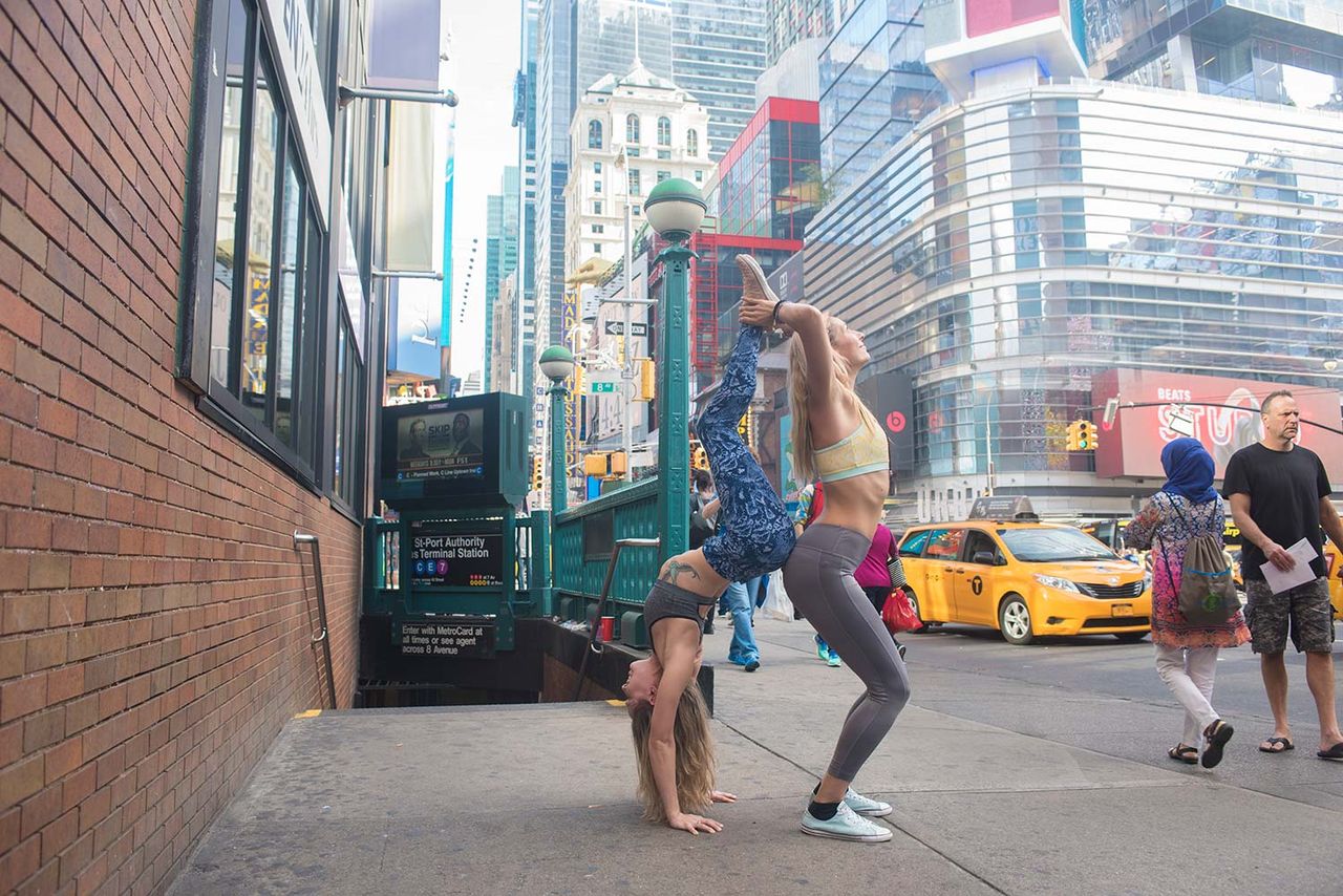 Woman doing a handstand on a city street lined with tall buildings and yellow taxis